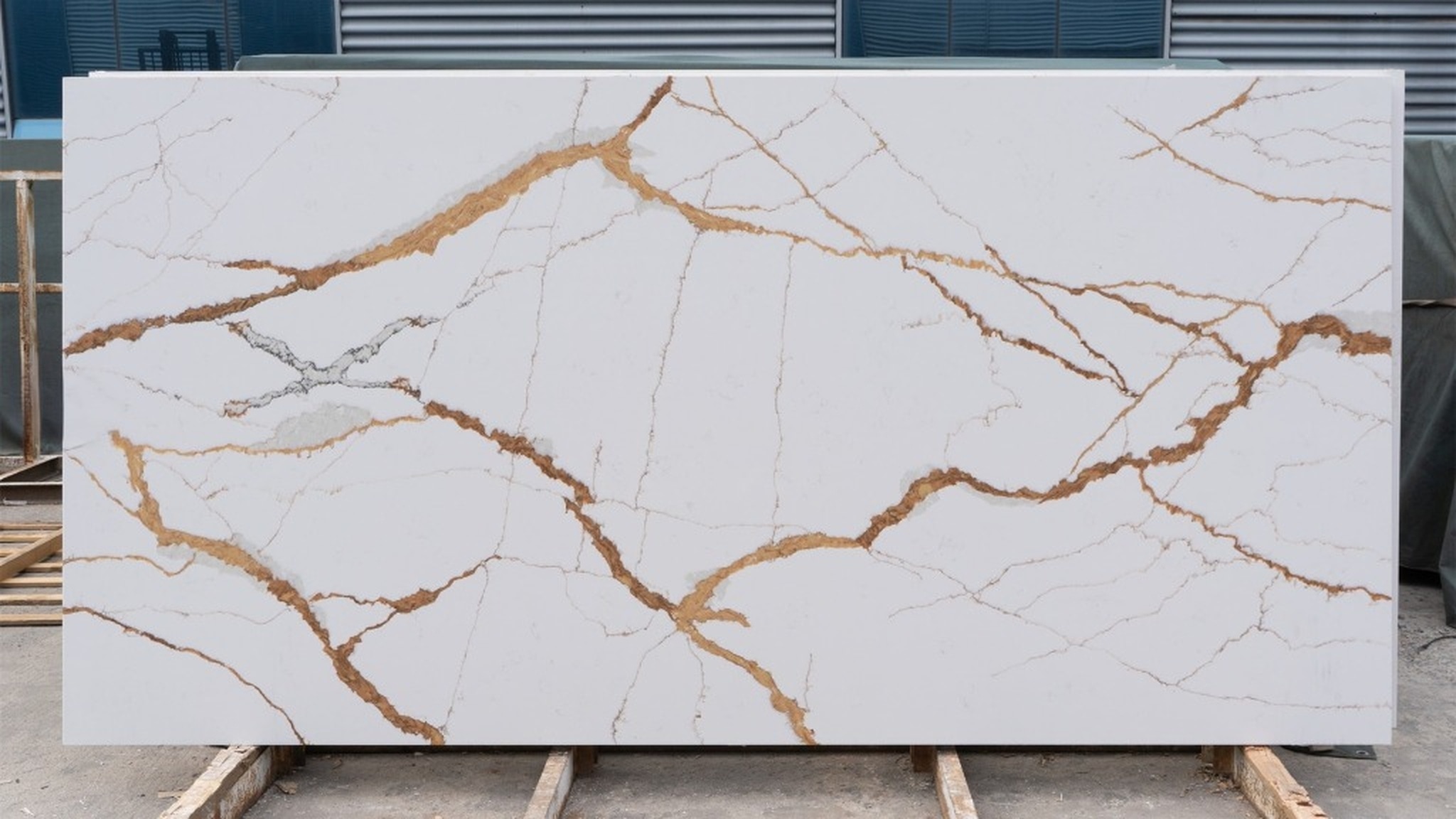 High-quality raw Calacatta gold quartz slab sitting on A-frame inside a modern countertop fabrication shop, ready for CNC cutting.